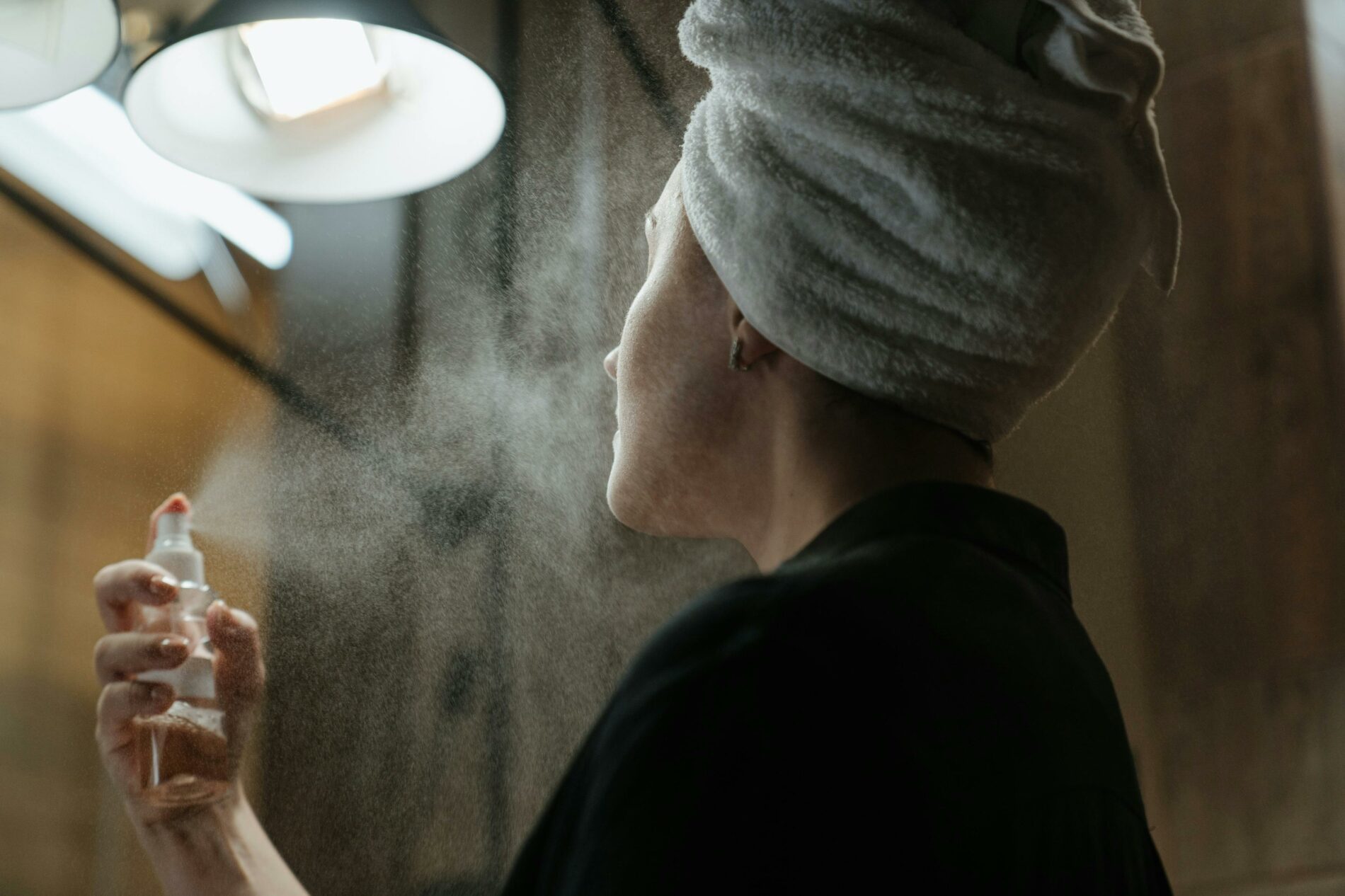 Femme qui se vaporise un produit sur le visage, pratiquant sa routine du soir pour un meilleur sommeil.