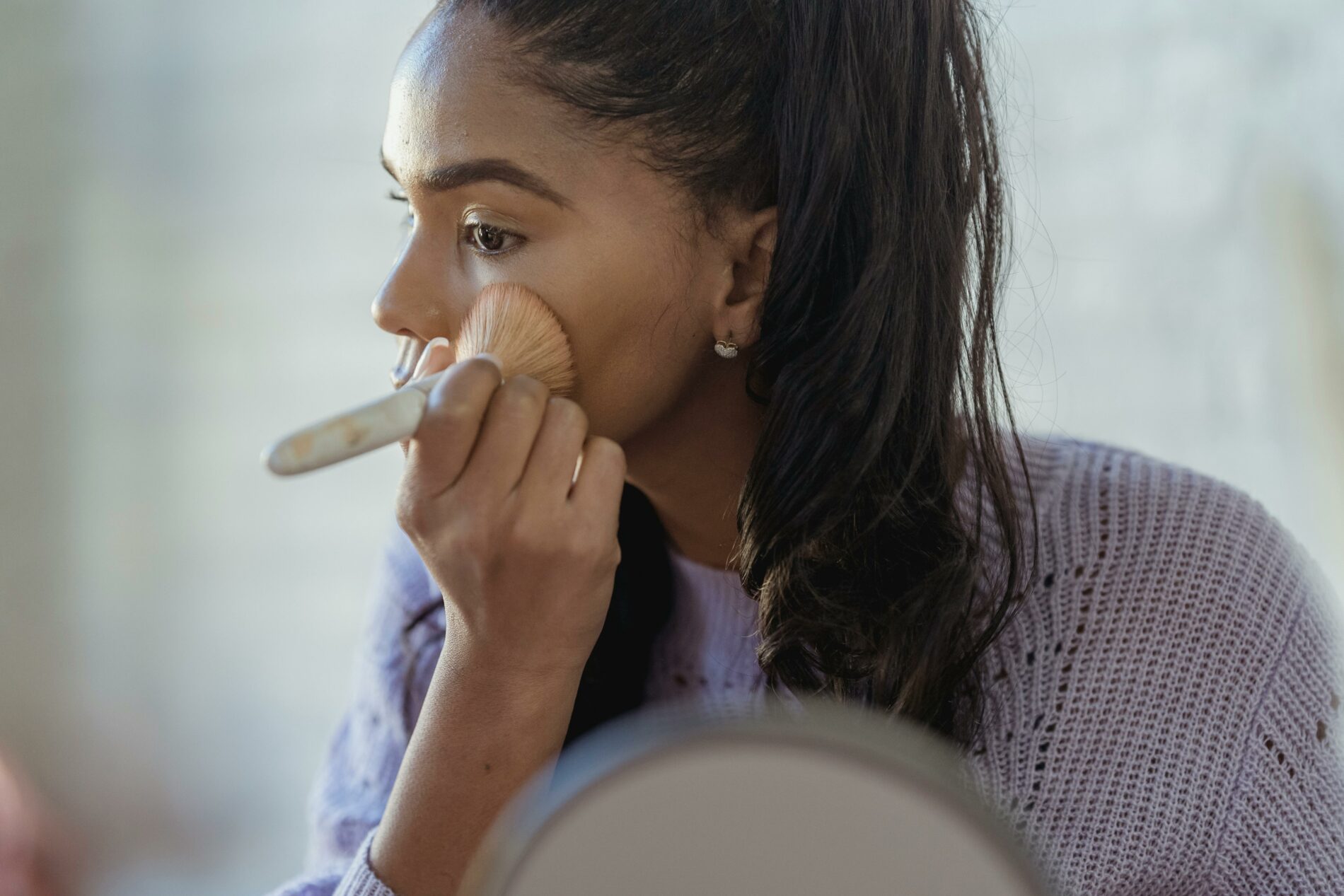 Femme avec un pinceau sur le visage, en train de réaliser une routine de soin.