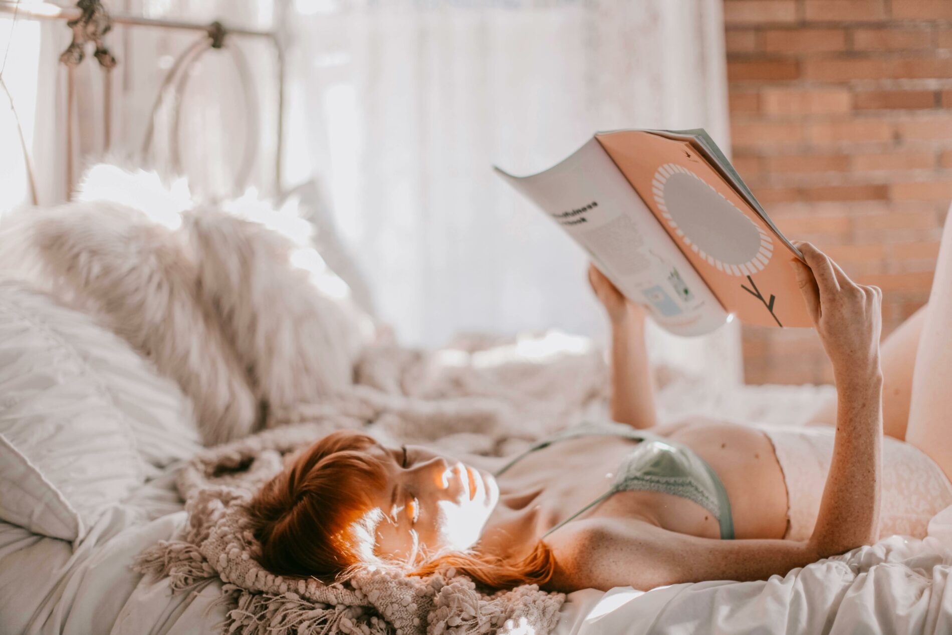 Femme en lingerie, qui lit un livre sur son lit, dans une ambiance douce et paisible.